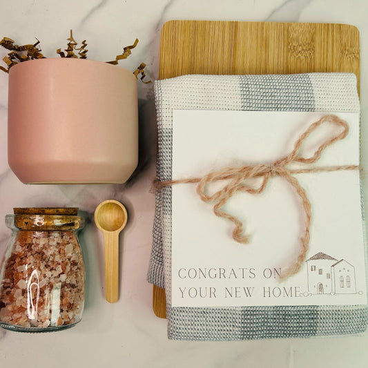 A jar of pink Himalayan salt with a small wooden spoon, a cutting board, and a checkered dish towel, tied together with twine, placed on a kitchen counter. real estate gift, gift for clients, realtor