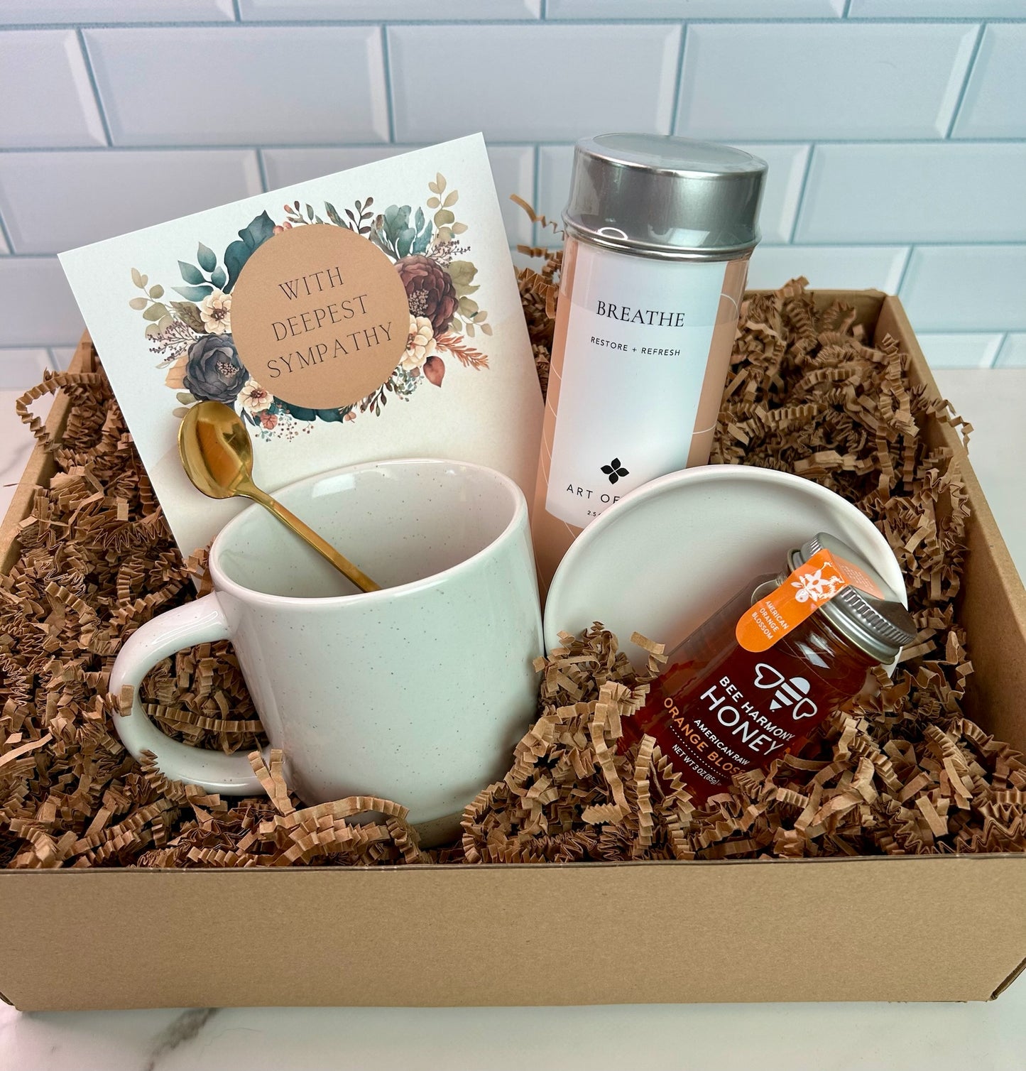 A deluxe sympathy gift box containing a speckled mug, a jar of Breathe herbal tea, a spoon.