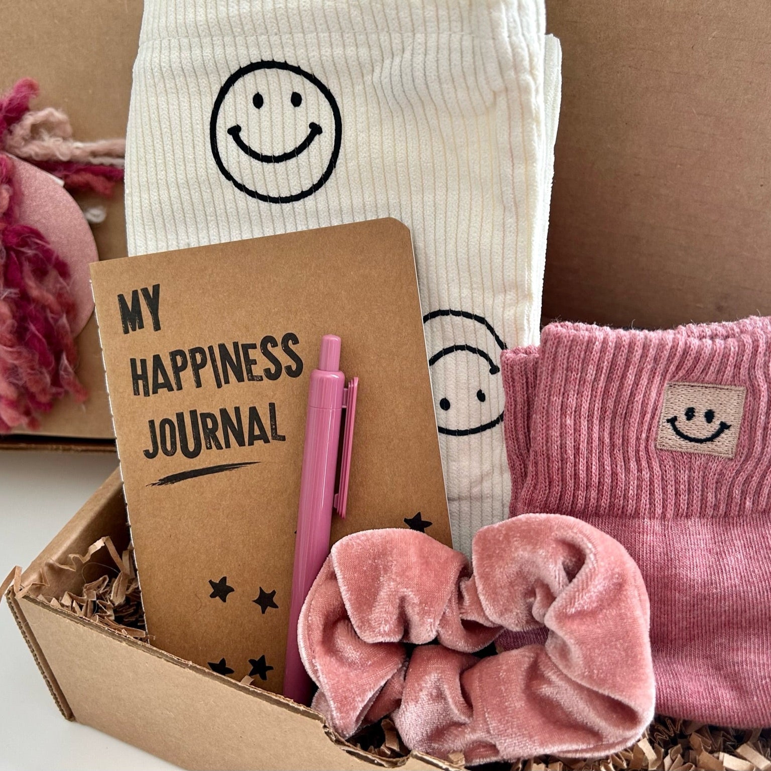 Box containing a happiness journal, pen, socks, and accessories with smiley face designs.