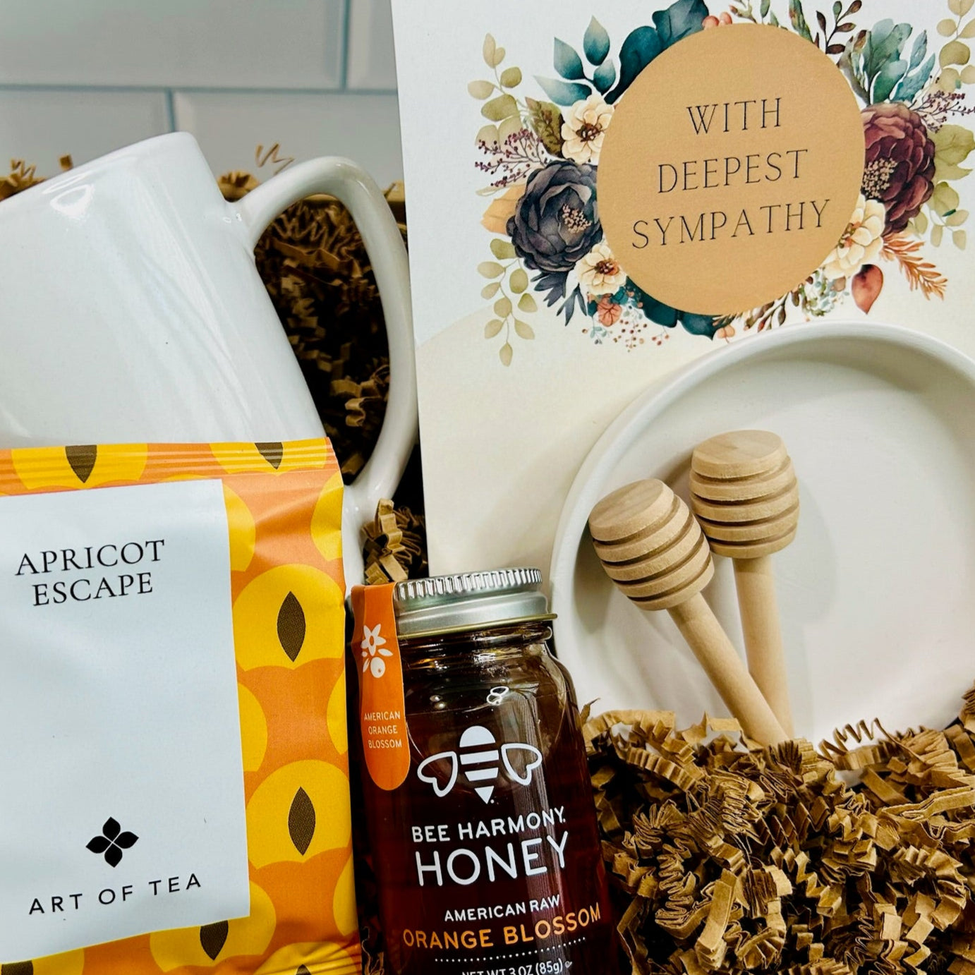 Tea package, honey jar, and sympathy card with floral design on a white surface.