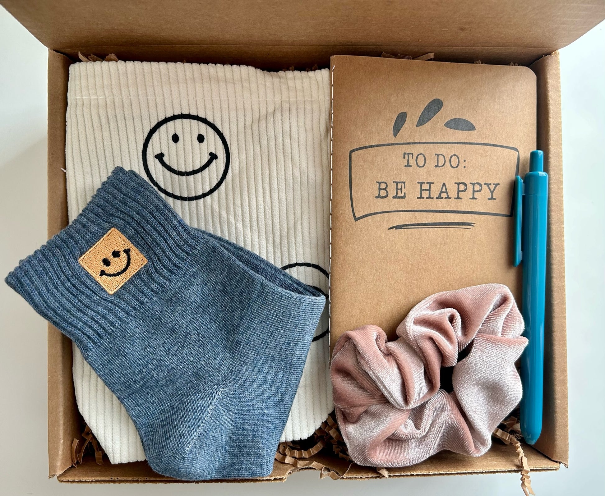 A thoughtful gift box to cheer someone up. Includes a happiness notebook, a smiley face bag, a pen, a scrunchie, and smiley face socks. 