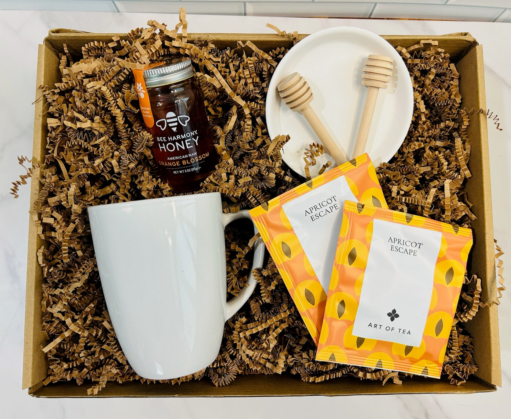 Top picture of a sympathy gift box including  ceramic mug, honey, herbal tea, honey stir sticks, and a sympathy card. 